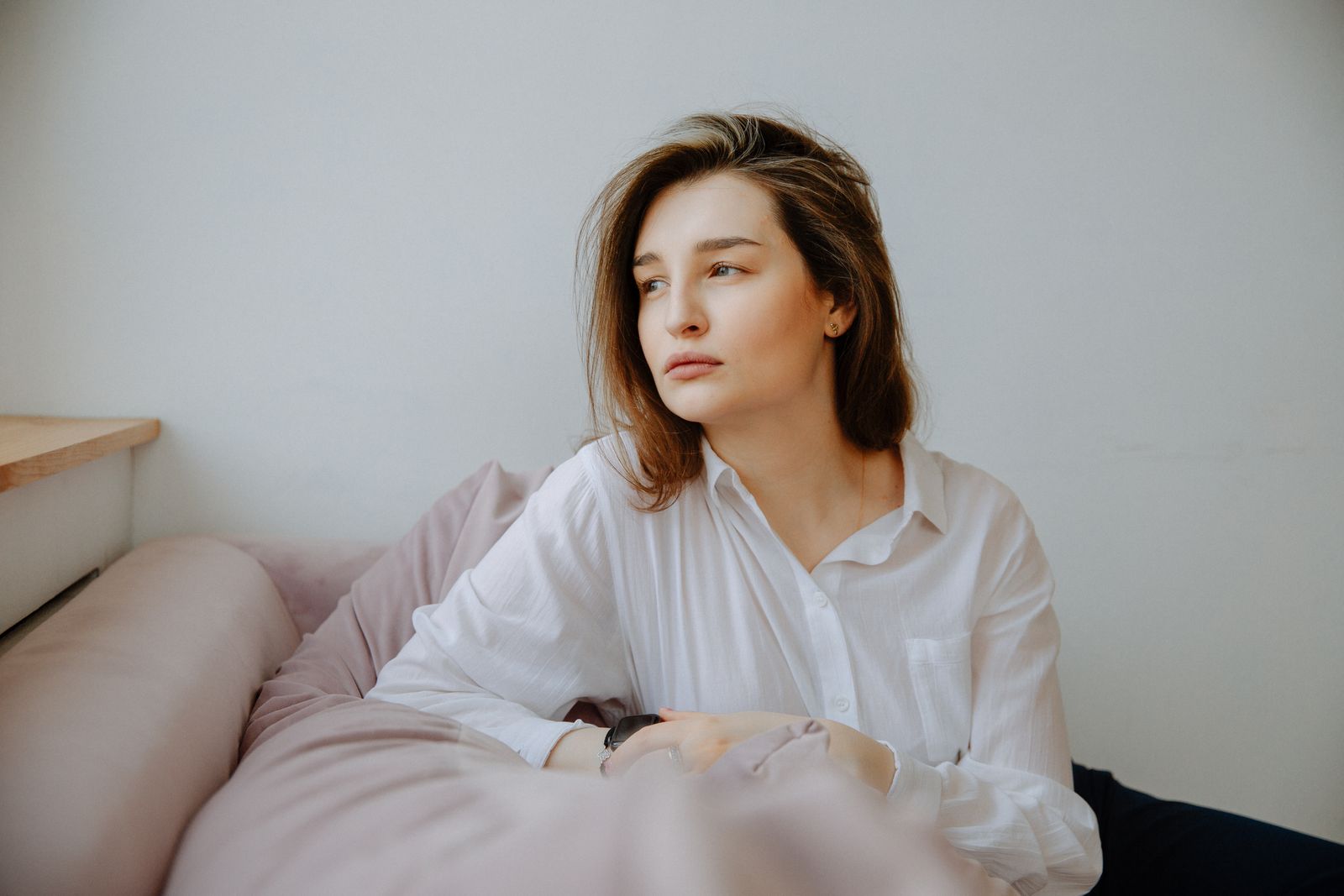 A contemplative woman in a white blouse sitting on a sofa, looking away.