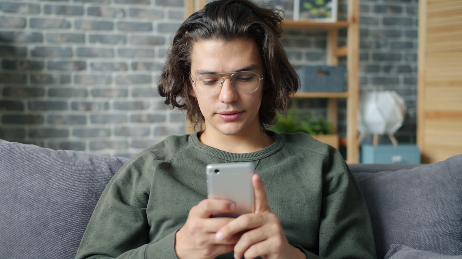Young man with glasses using a smartphone on couch.