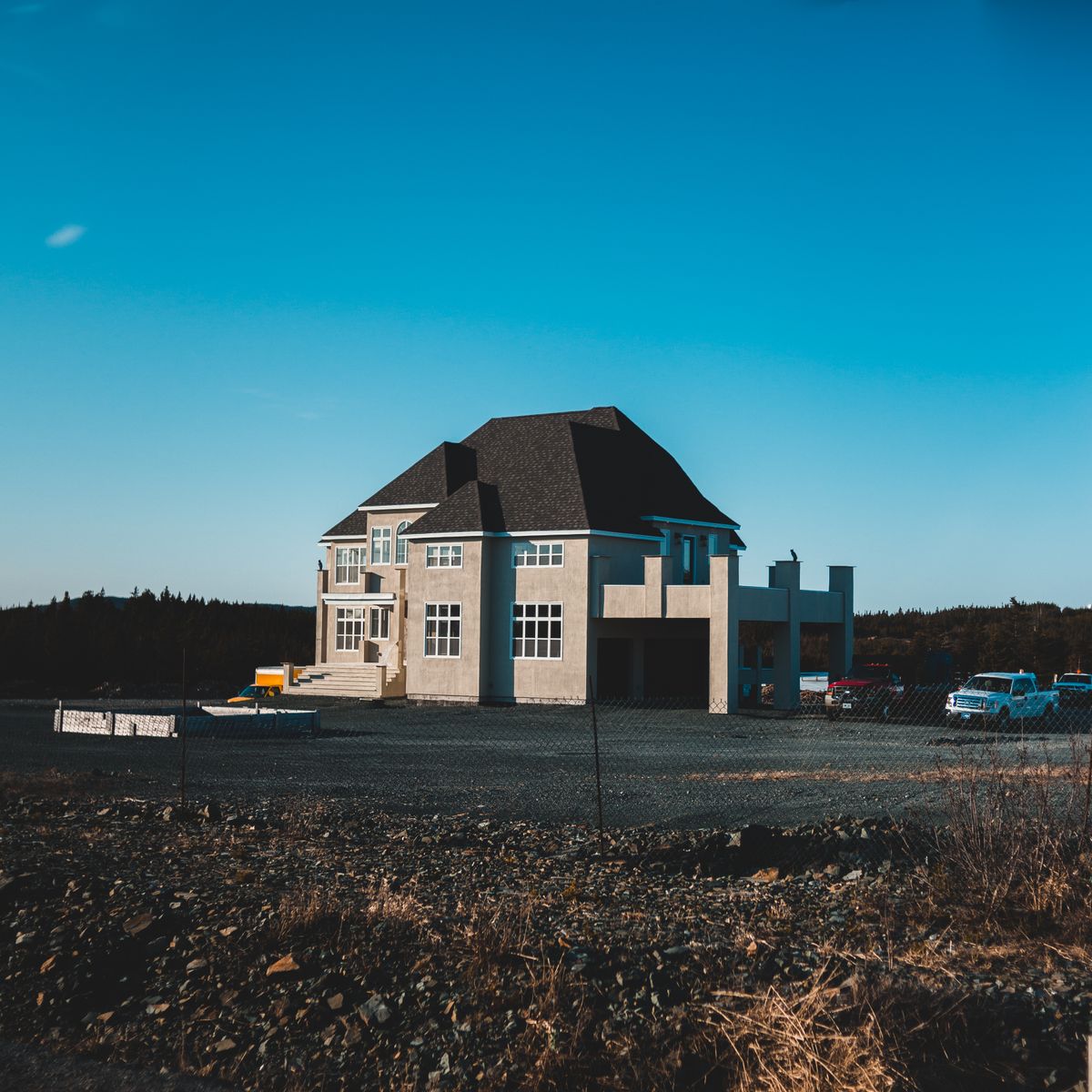 Exterior of old stone building near roadway with automobile and pebble roadside with dry grass under bright cloudless sky in autumn