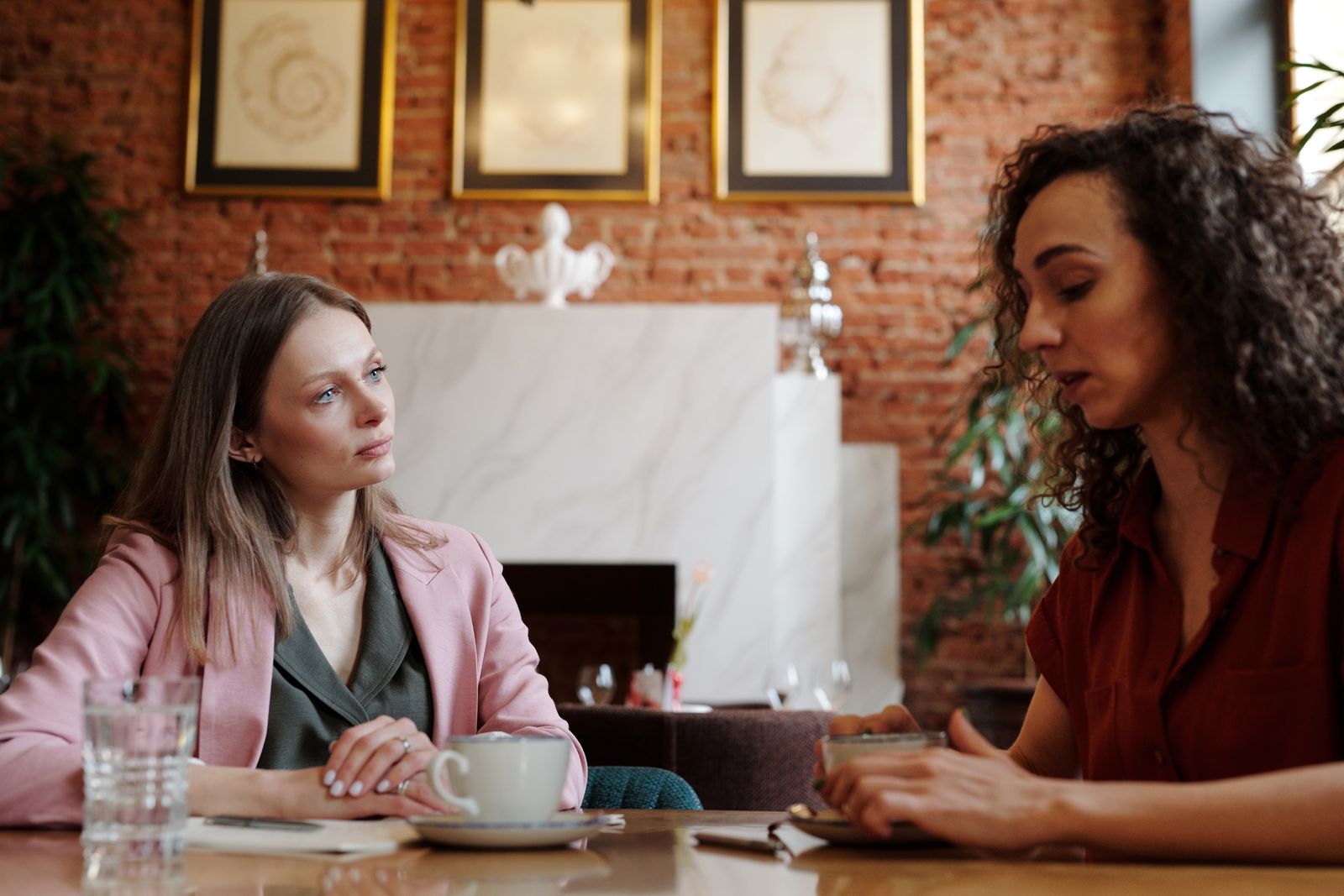 Two women engaged in serious discussion over coffee in a cozy indoor café setting.