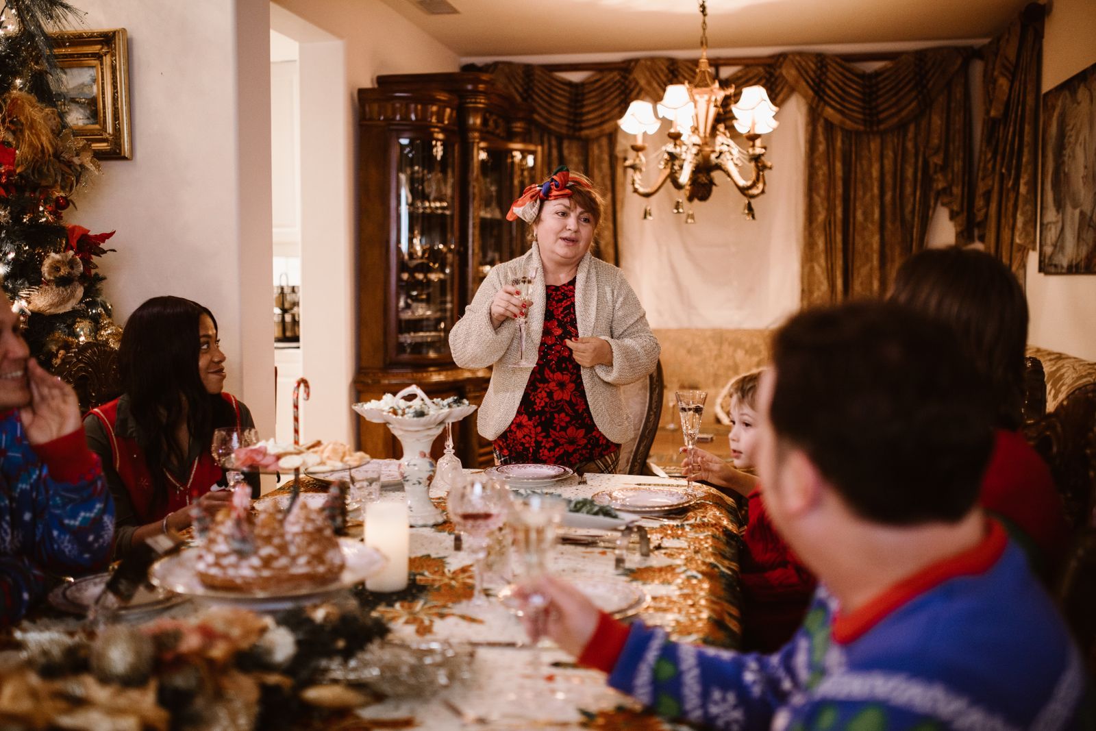 Family gathered indoors enjoying a traditional festive dinner with a toast by the host.