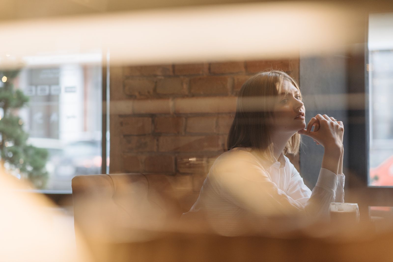 Woman in white shirt gazing thoughtfully in urban cafe with exposed brick interior.