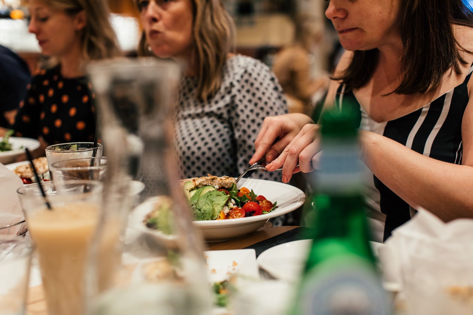 Friends sharing a lively meal at a restaurant, featuring fresh salads and drinks.