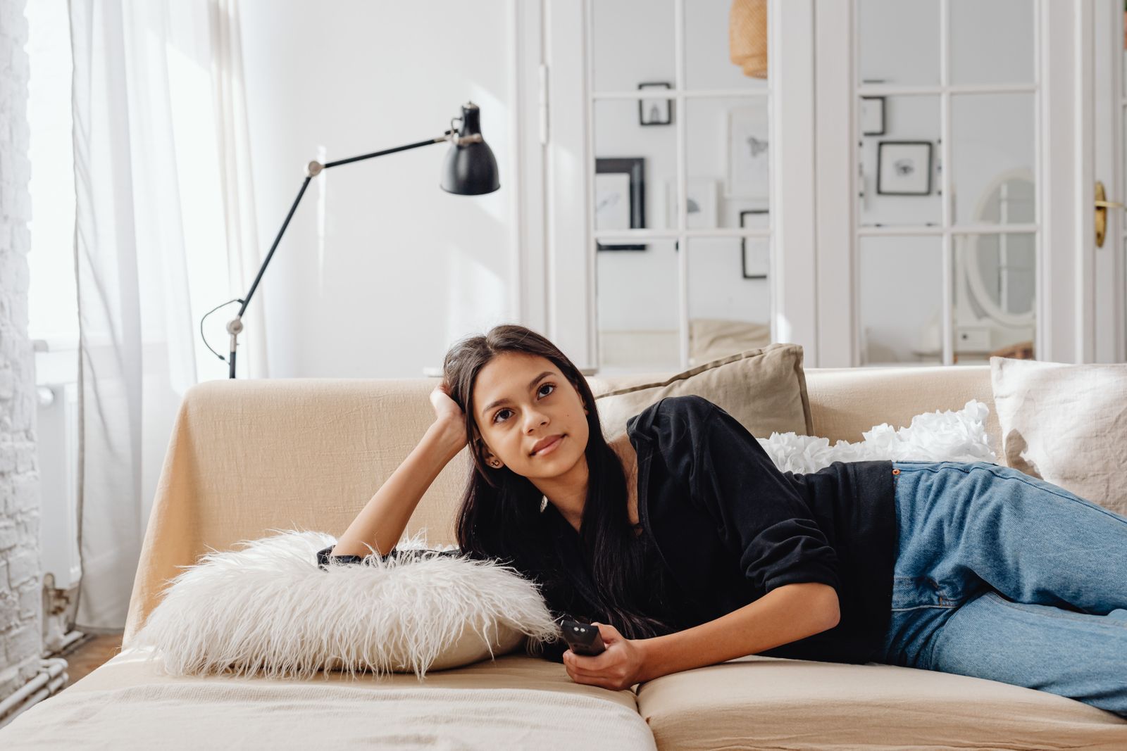 Woman lounging comfortably on a sofa with a remote control, enjoying leisure time indoors.