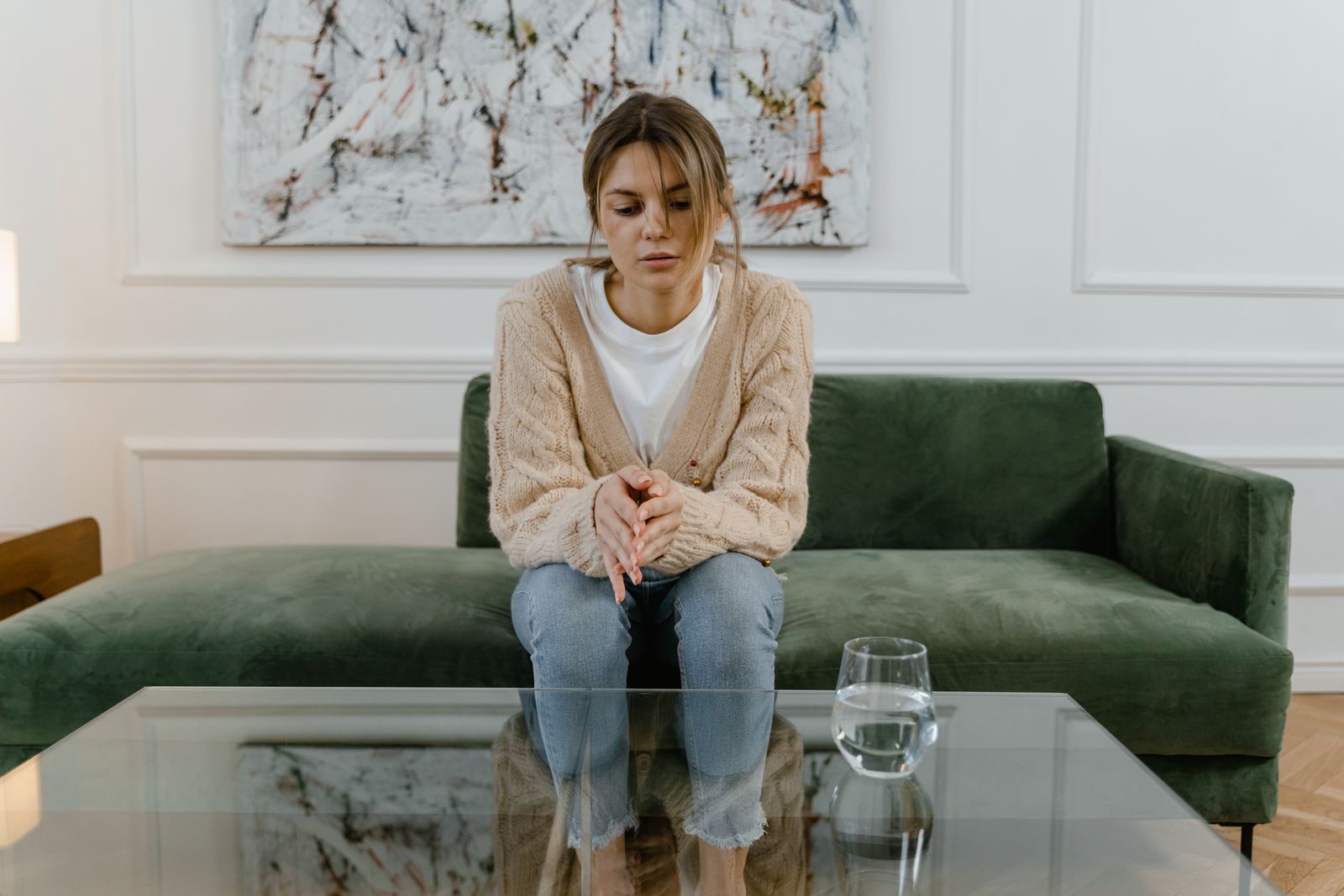 Woman sitting on a green sofa with a pensive expression, reflecting indoors.