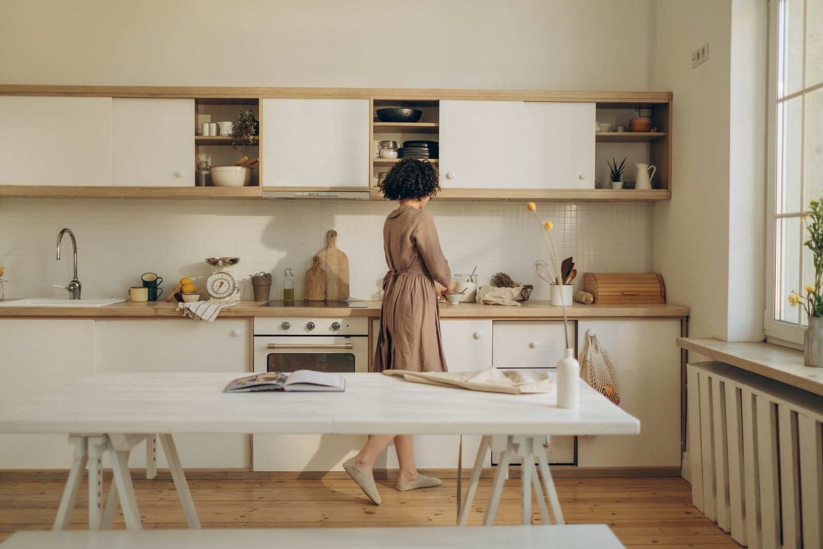 A woman casually cooking in a minimalist kitchen with natural light.