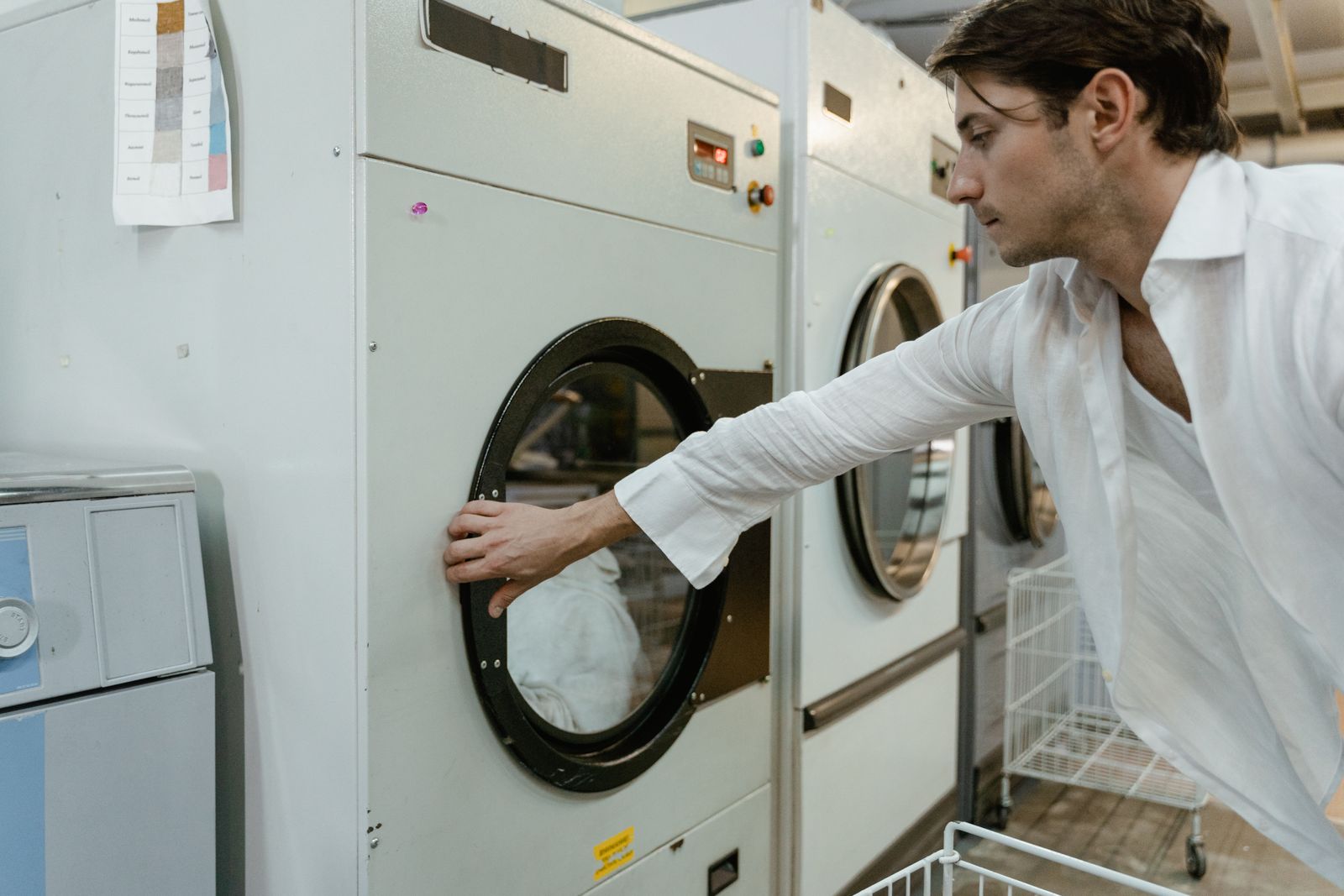 An adult man wearing a white shirt using a washing machine in a modern laundry facility.