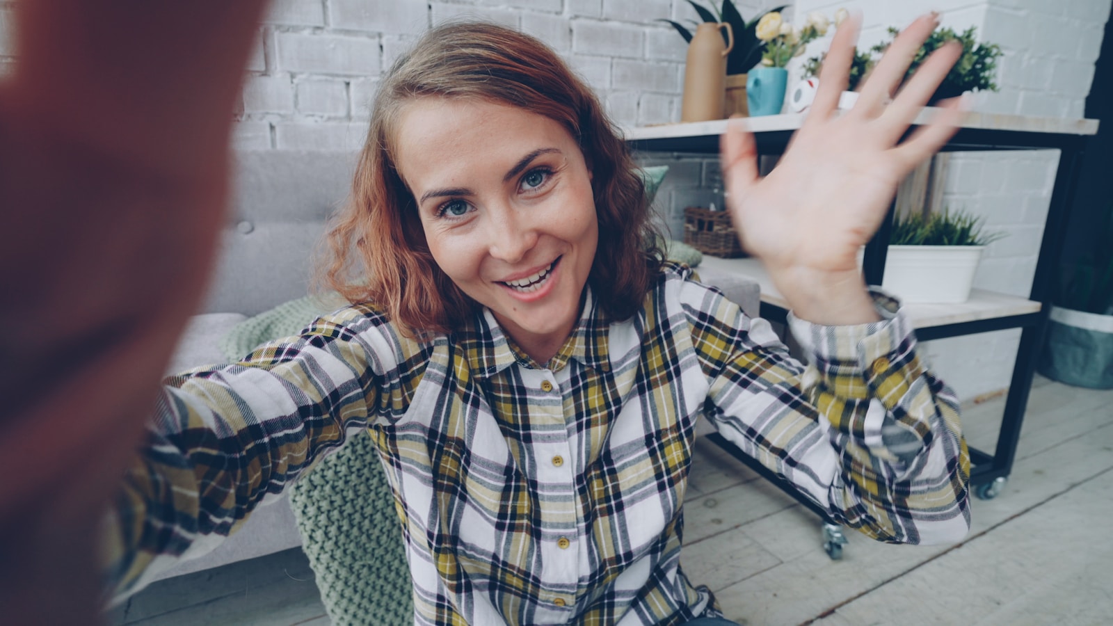 Woman waves hello while taking a selfie
