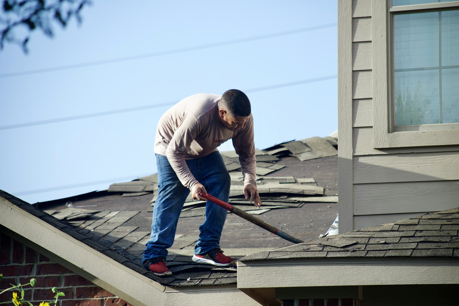 A person in a long-sleeved shirt removing shingles from a residential roof