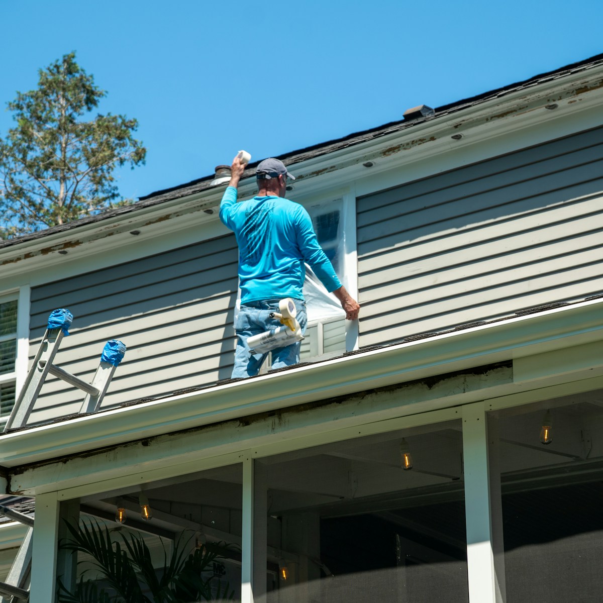 A person in a blue shirt taping plastic over a window on a roof