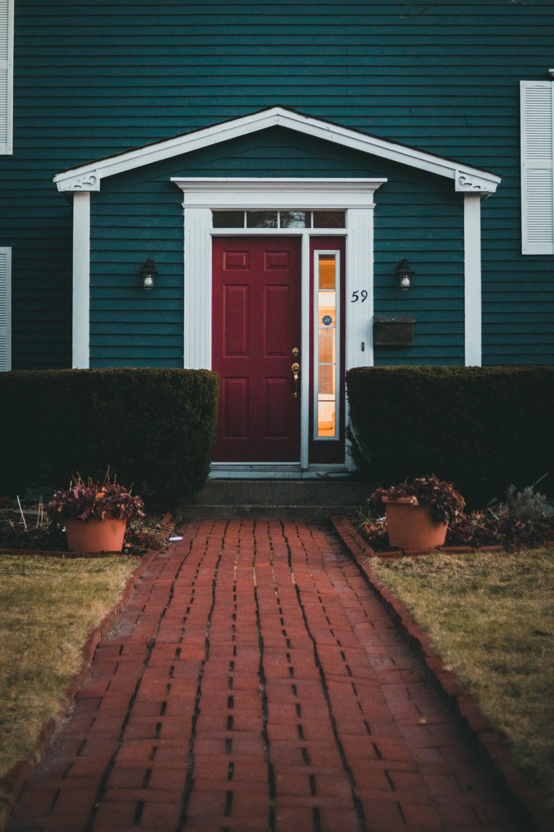 A captivating view of a red door entrance with brick walkway and bushes in a suburban setting.