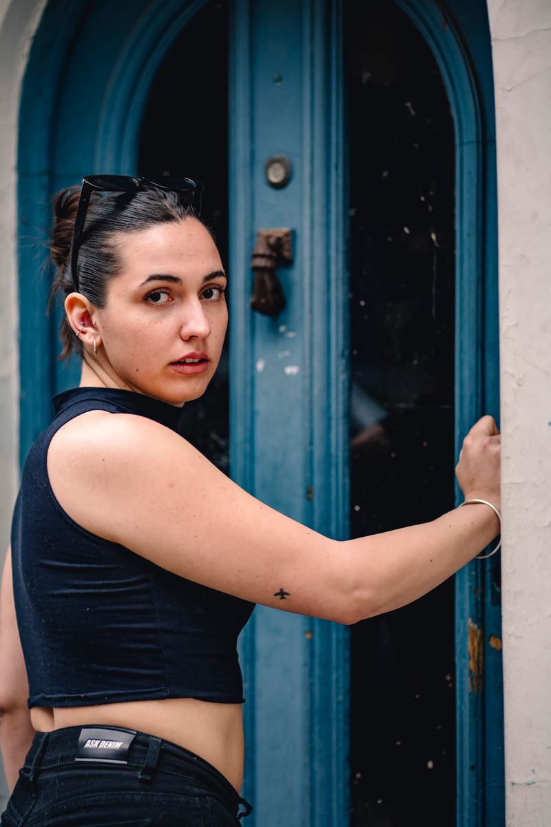 A stylish woman in black stands near a vibrant blue door, showcasing urban fashion vibes.