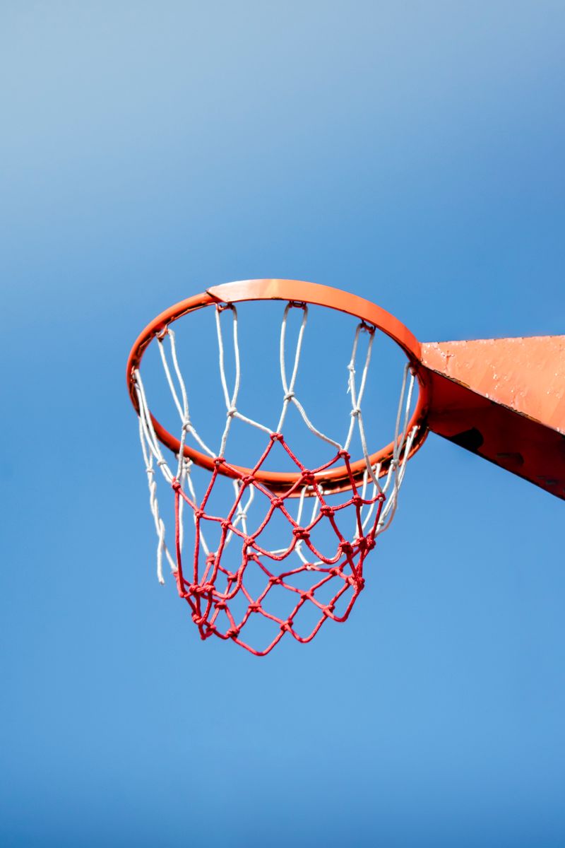 Orange basketball hoop and net against a vibrant blue sky, capturing the essence of outdoor sports.