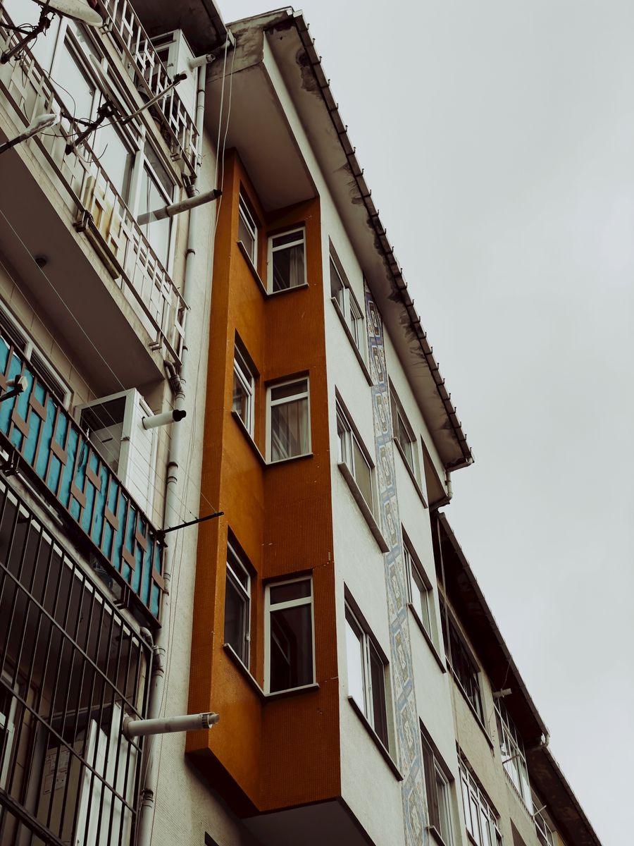 A street view of urban apartments with a striking orange facade under a cloudy sky.