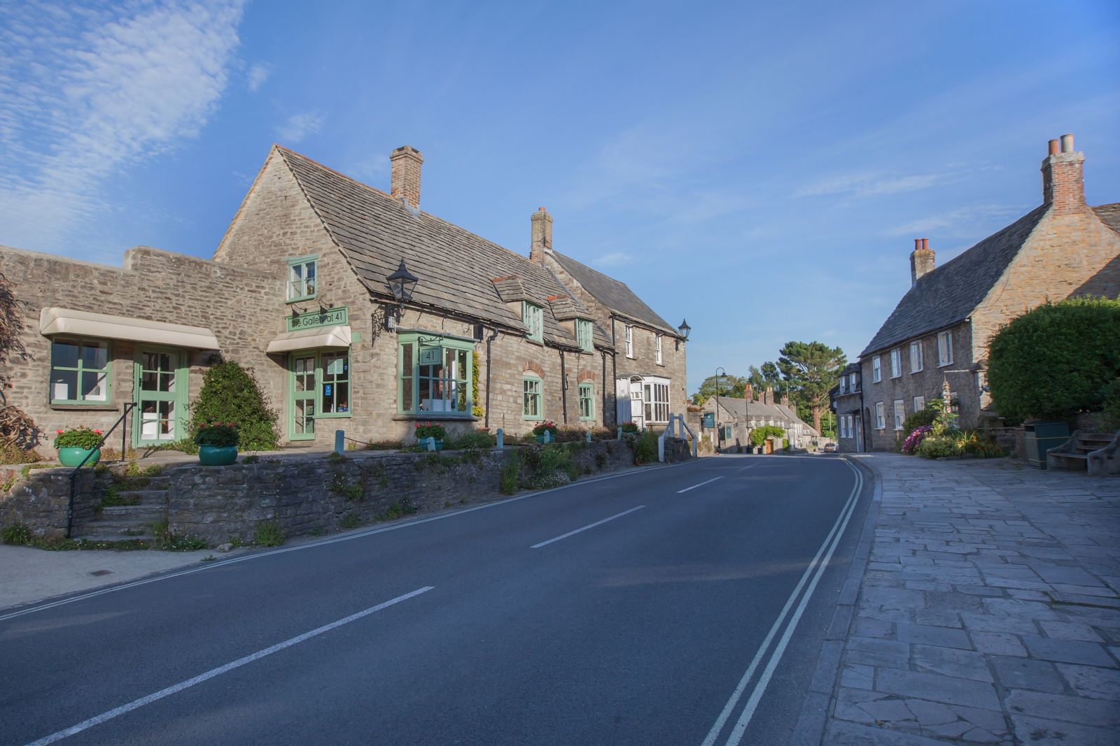 Quaint village street with historic stone buildings in Dorset, England under a clear blue sky.