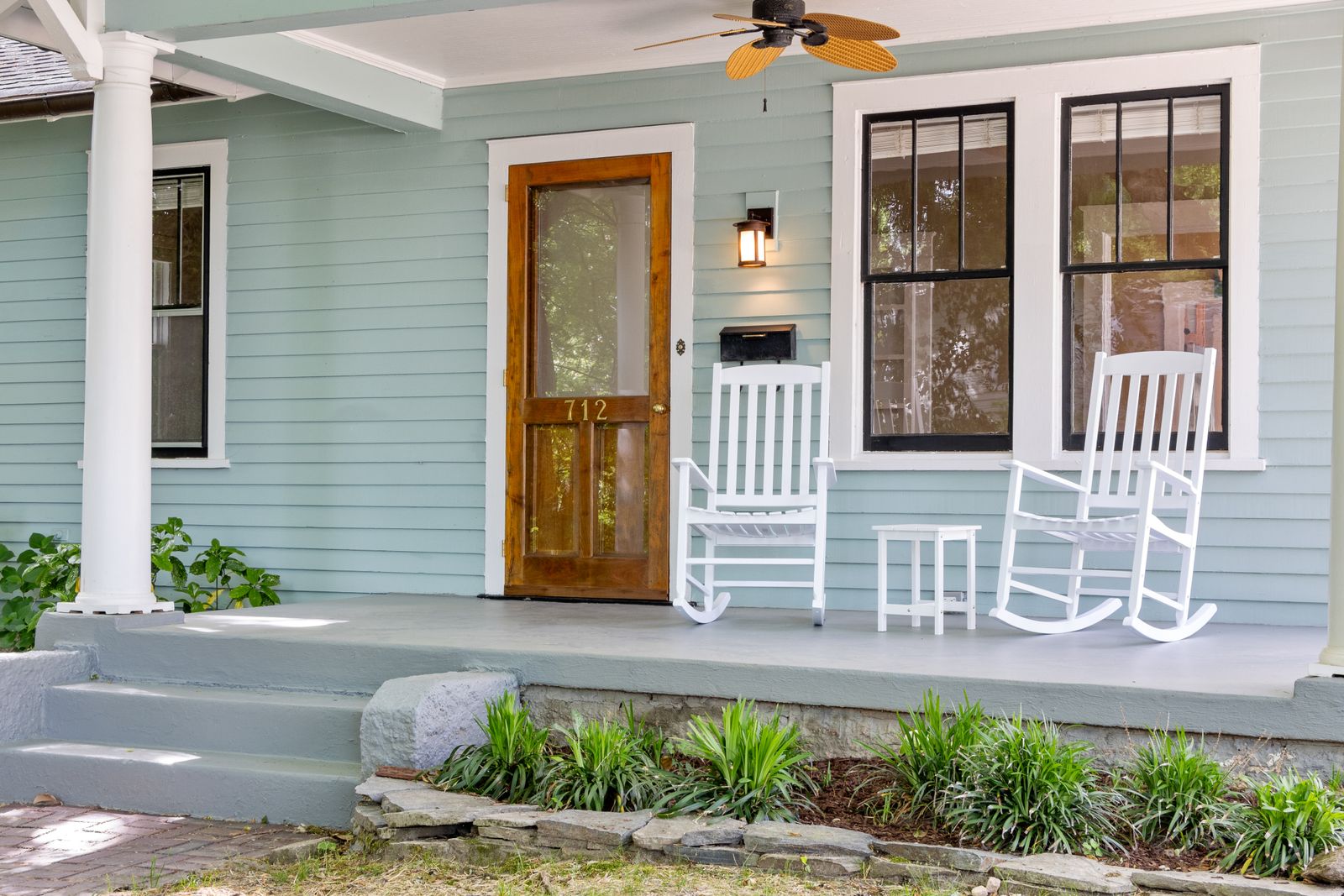 Inviting front porch featuring white rocking chairs and a wooden door, perfect for relaxation.