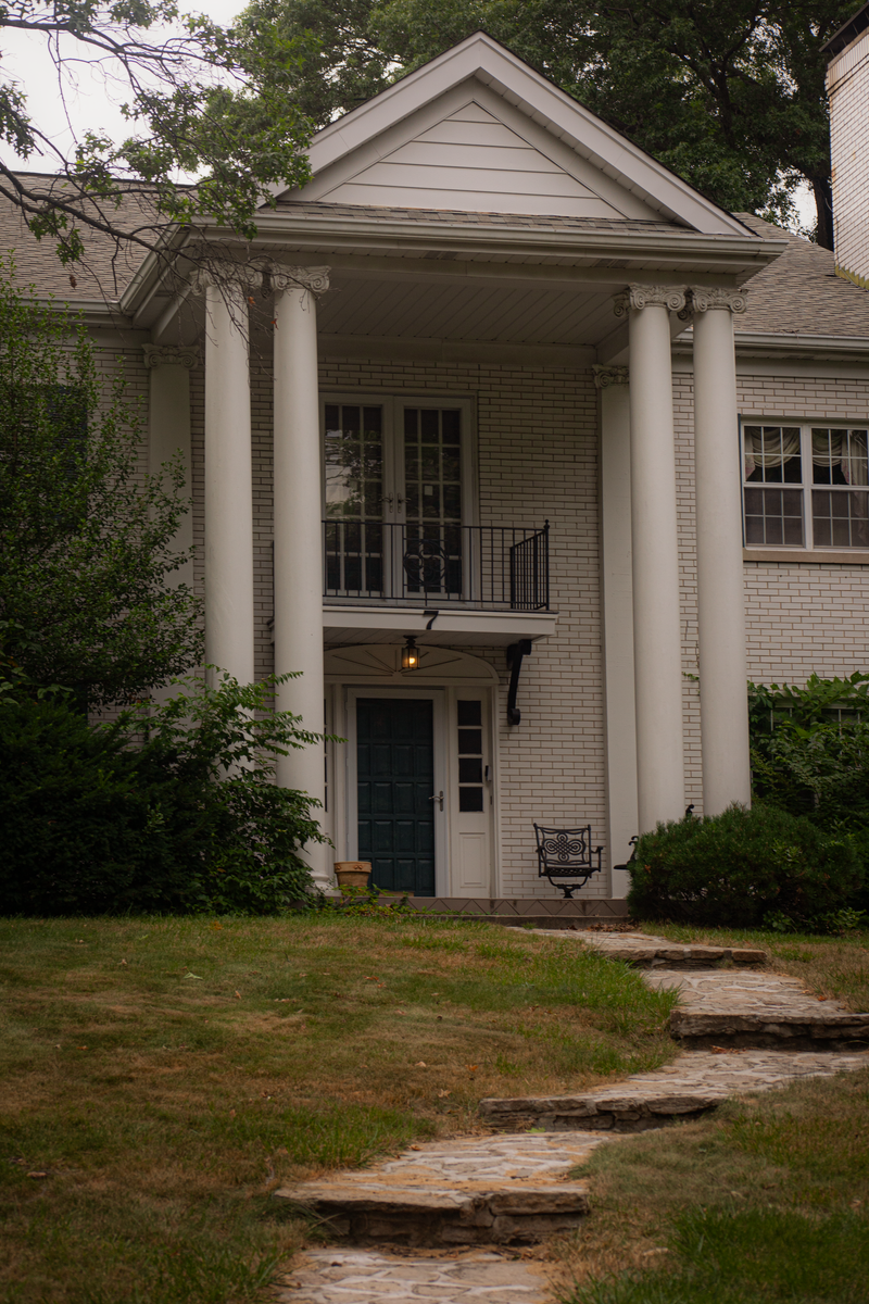 Front view of a luxury Colonial style mansion with grand pillars and lush greenery.