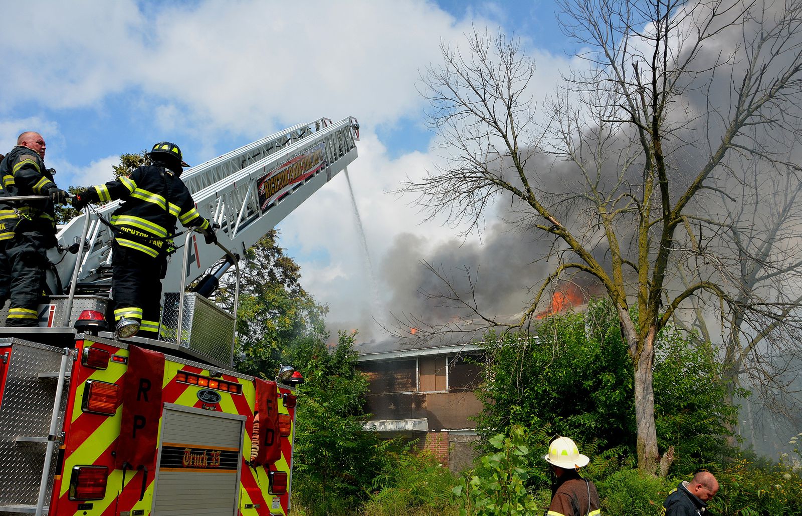 Firefighters in action on ladder truck extinguishing a house blaze outdoors.