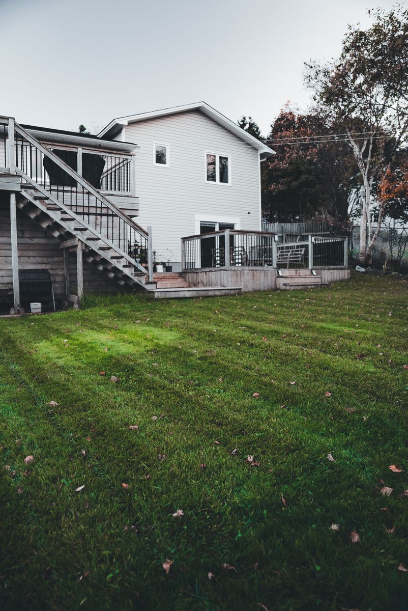 White house with a wooden deck overlooking a well-maintained spacious green backyard.