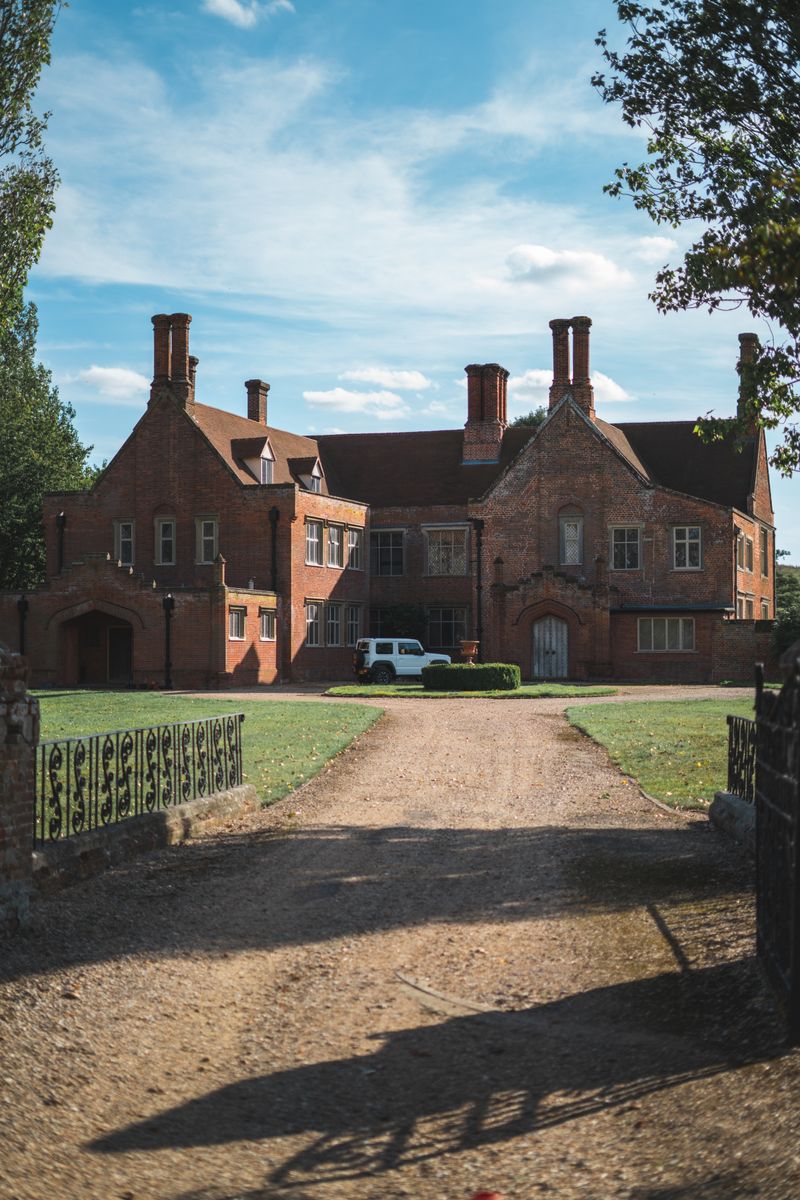 An elegant brick mansion with a large driveway and surrounding lawn under a clear sky.