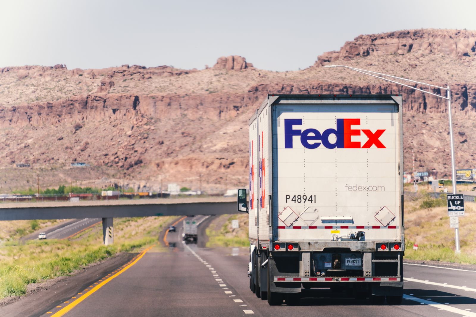 A FedEx truck travels on a scenic highway through Arizona's desert landscape under a clear sky.