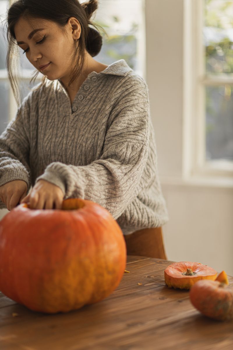 A woman in a cozy sweater carving a pumpkin indoors, capturing the essence of fall.