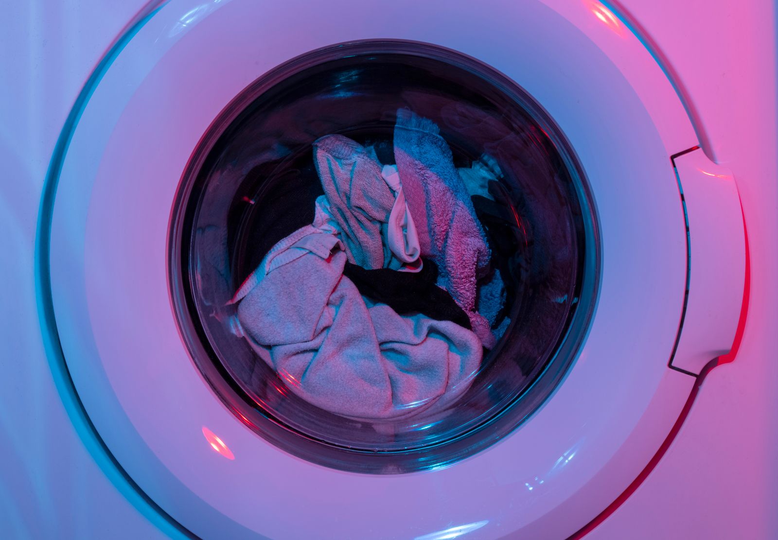 Colorful washing machine with clothes inside, lit by vivid purple and blue lights.