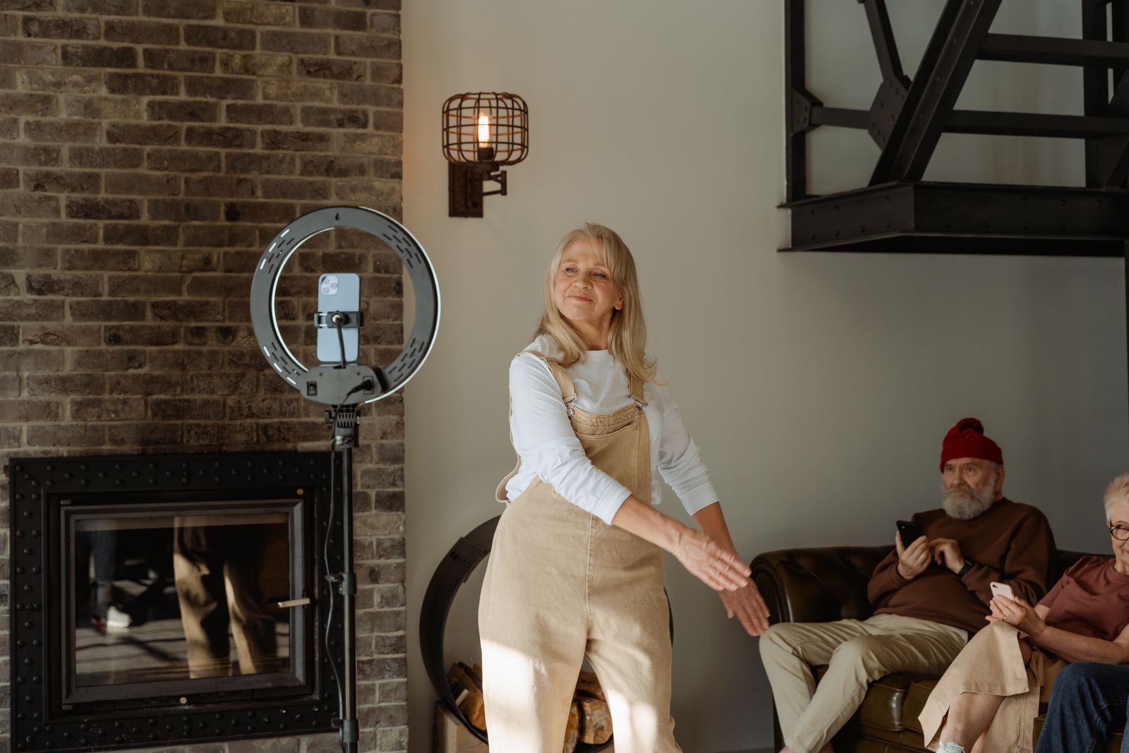 Cheerful senior woman dancing by a fireplace indoors, accompanied by friends.
