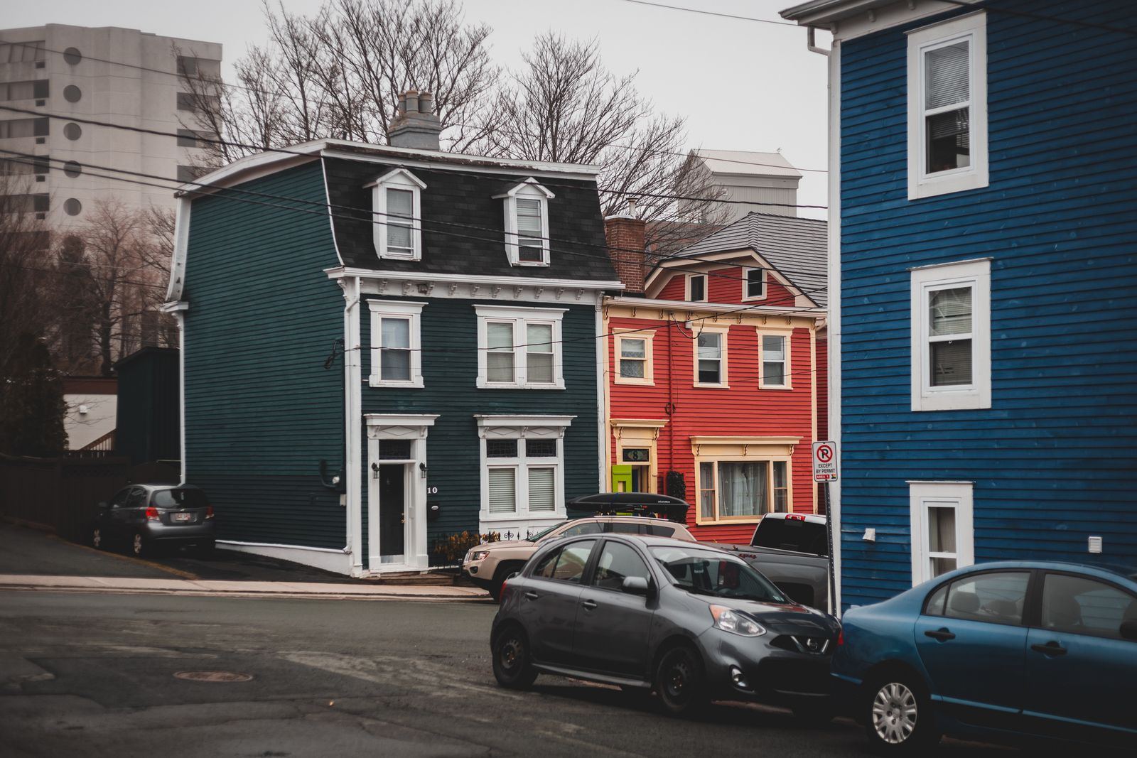 Colorful old fashioned residential houses located on street near asphalt road with parked automobiles in town with tall leafless trees