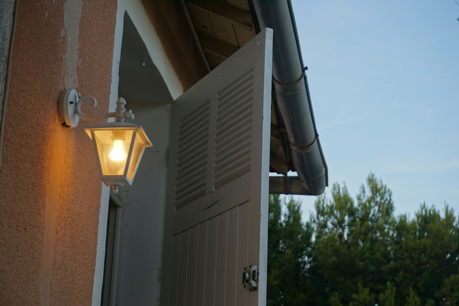 Outdoor lamp illuminates open white shutters on building