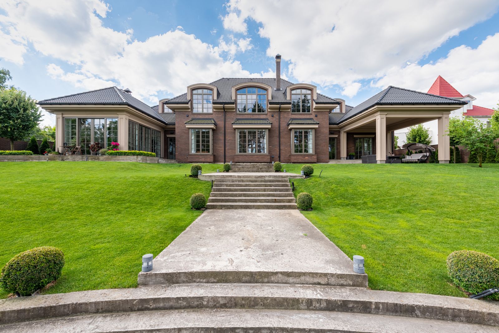 Elegant upscale mansion with lush green garden and clear blue sky.