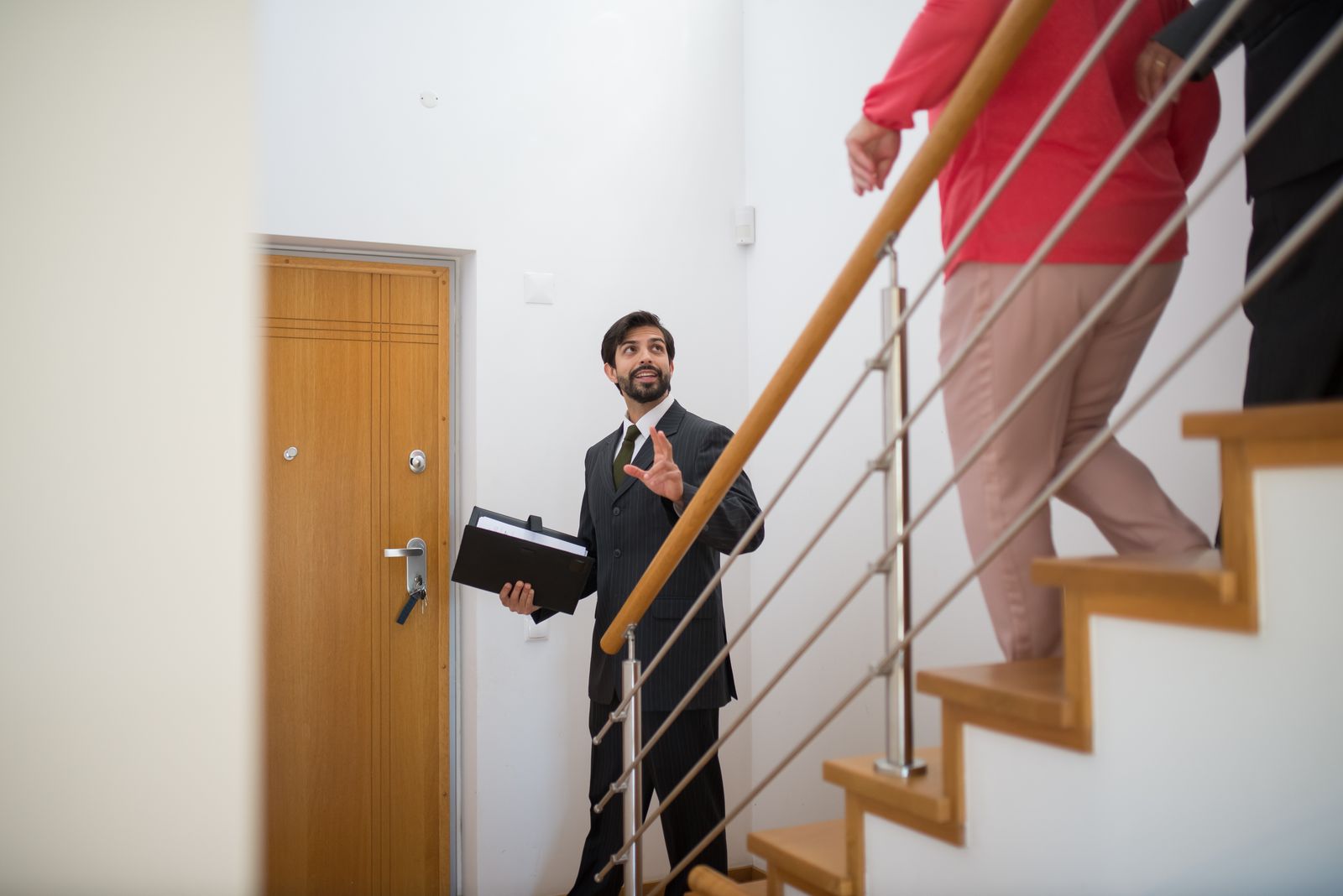 A realtor conducting a house tour with potential buyers on the stairs of a modern home.