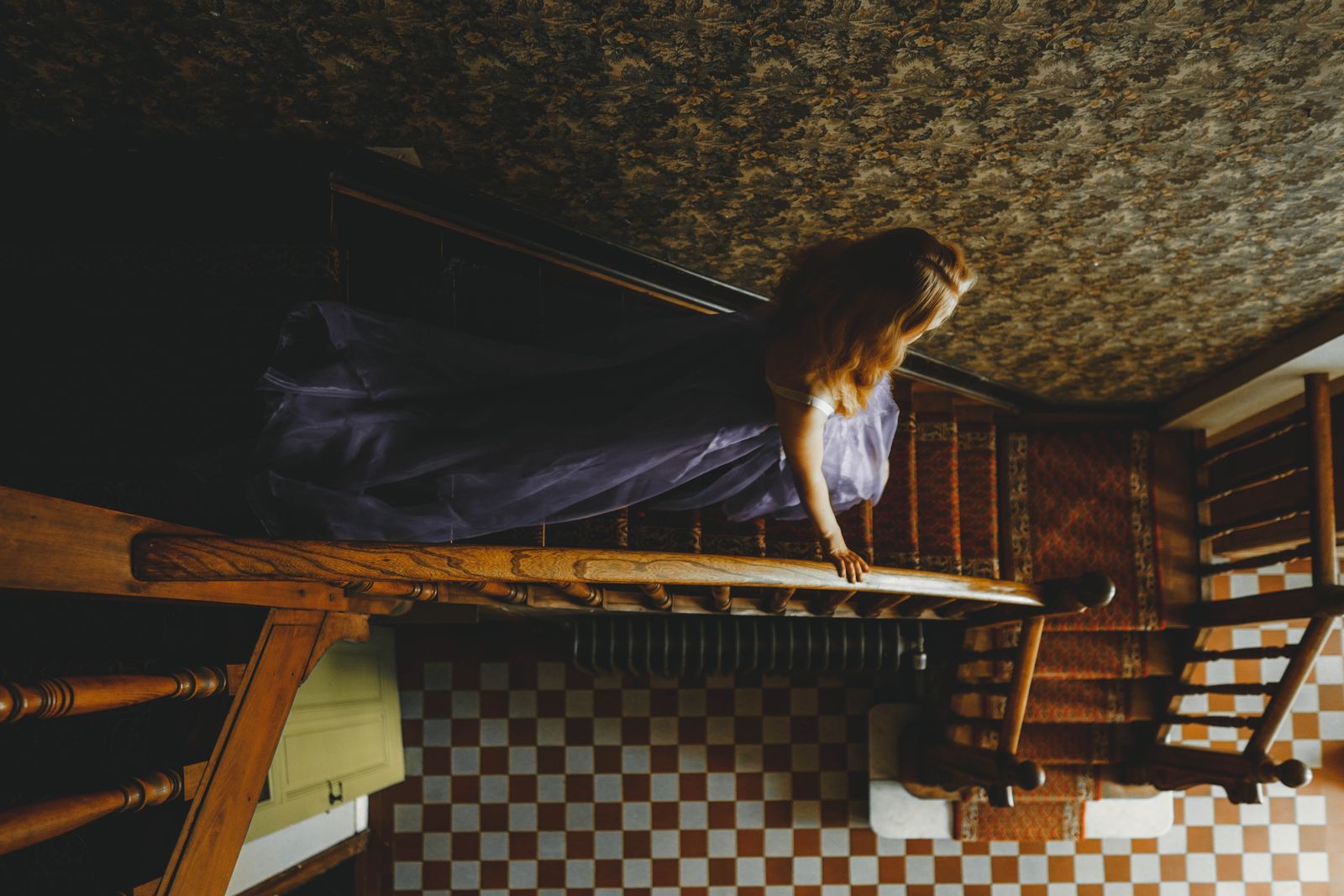 High angle view of a woman in a gown walking down a vintage staircase indoors.