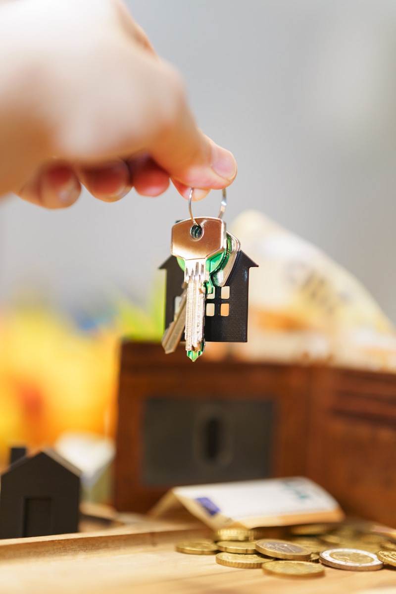 A hand holding keys with a house-shaped keychain over coins and a wallet