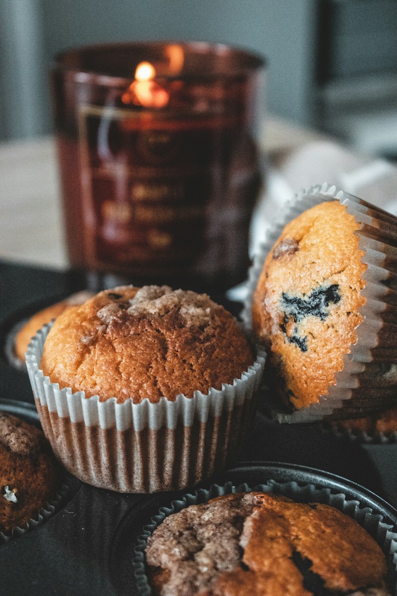 Blueberry muffins in paper liners with a lit candle in the background