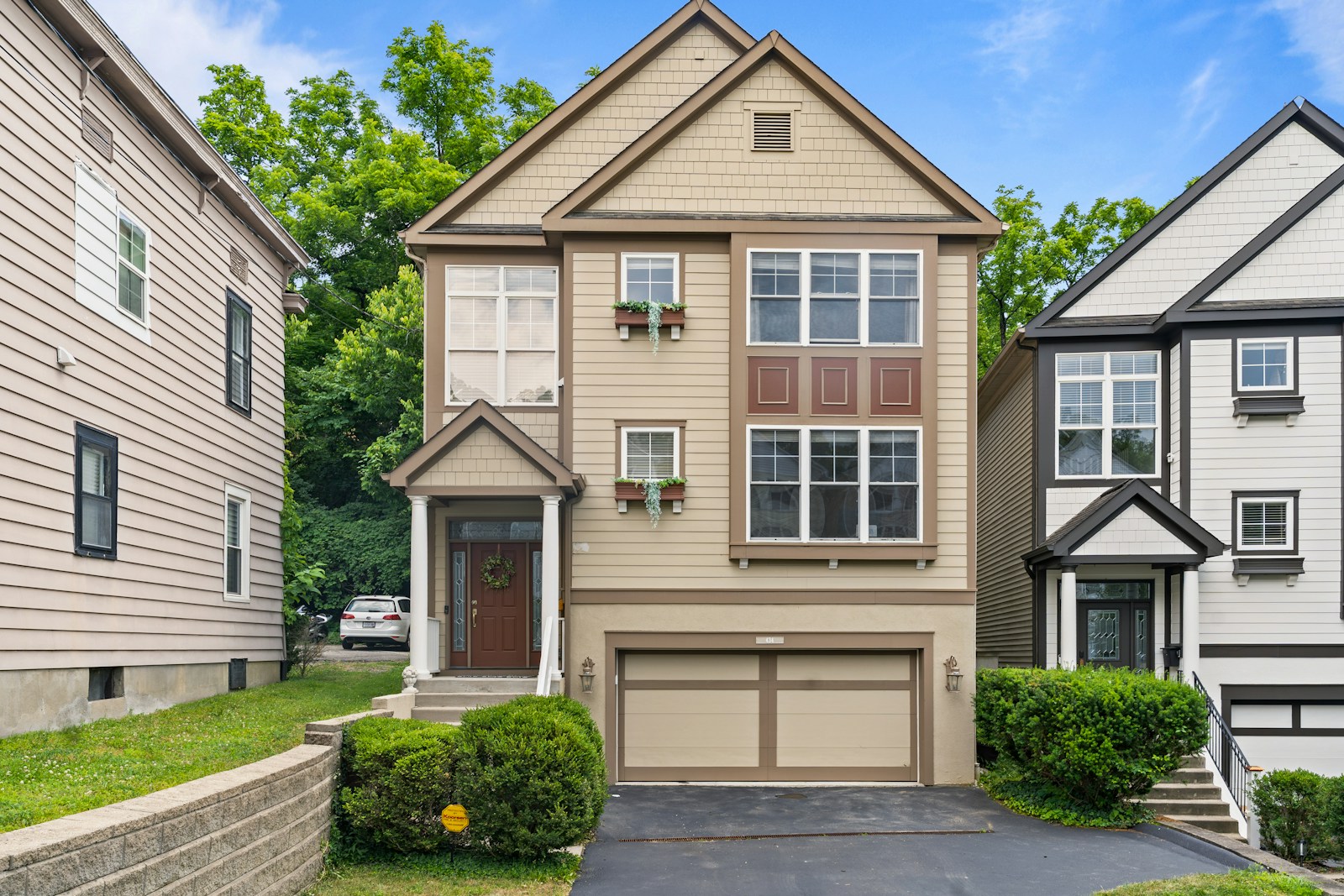 A beige multi-story house with a garage and green landscaping