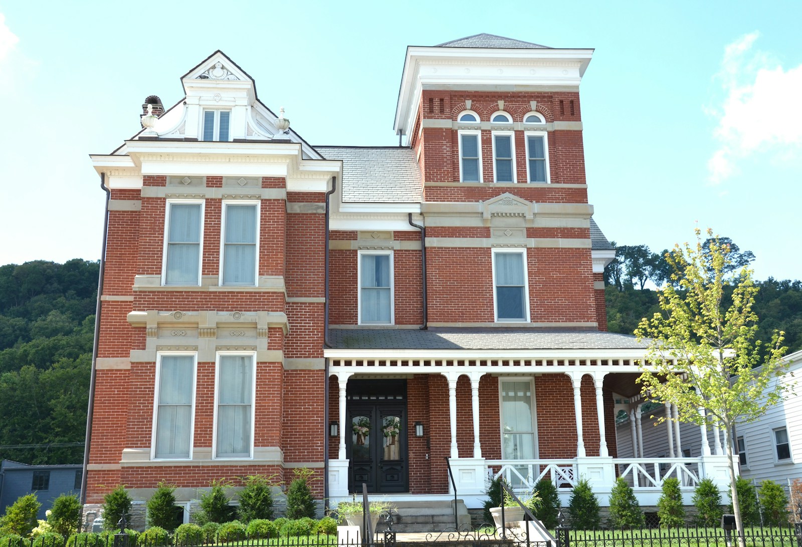 A red brick Victorian house with a white porch and a tall tower