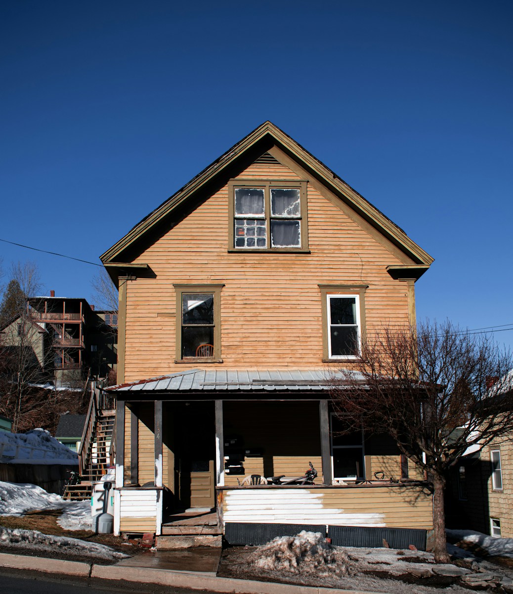 A two-story yellow house with a front porch and snow on the ground