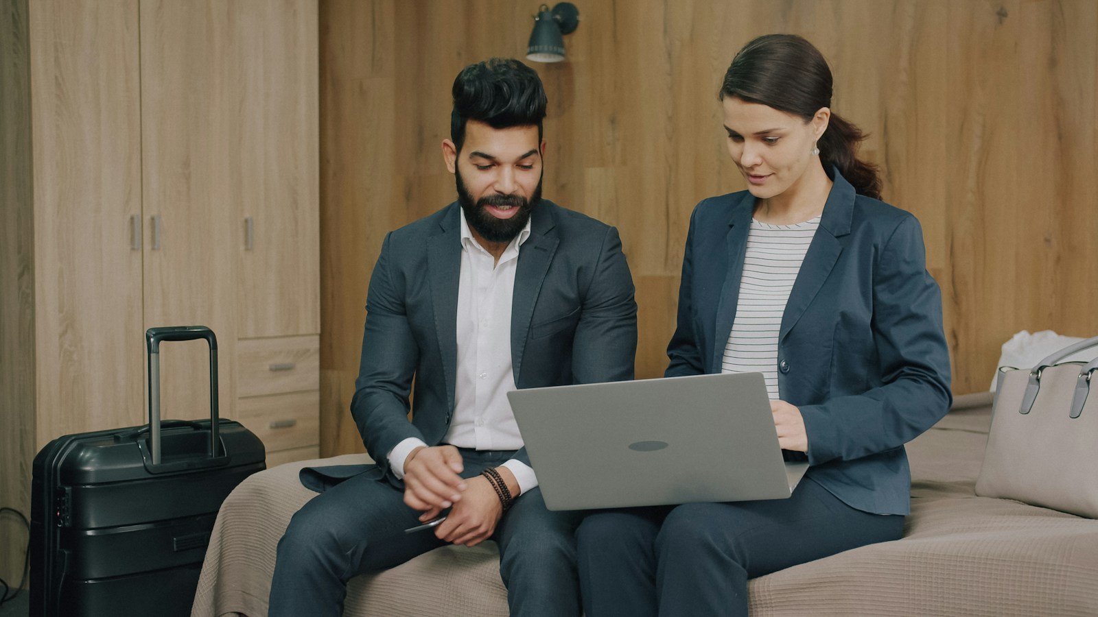 A man and a woman in business suits using a laptop on a hotel bed