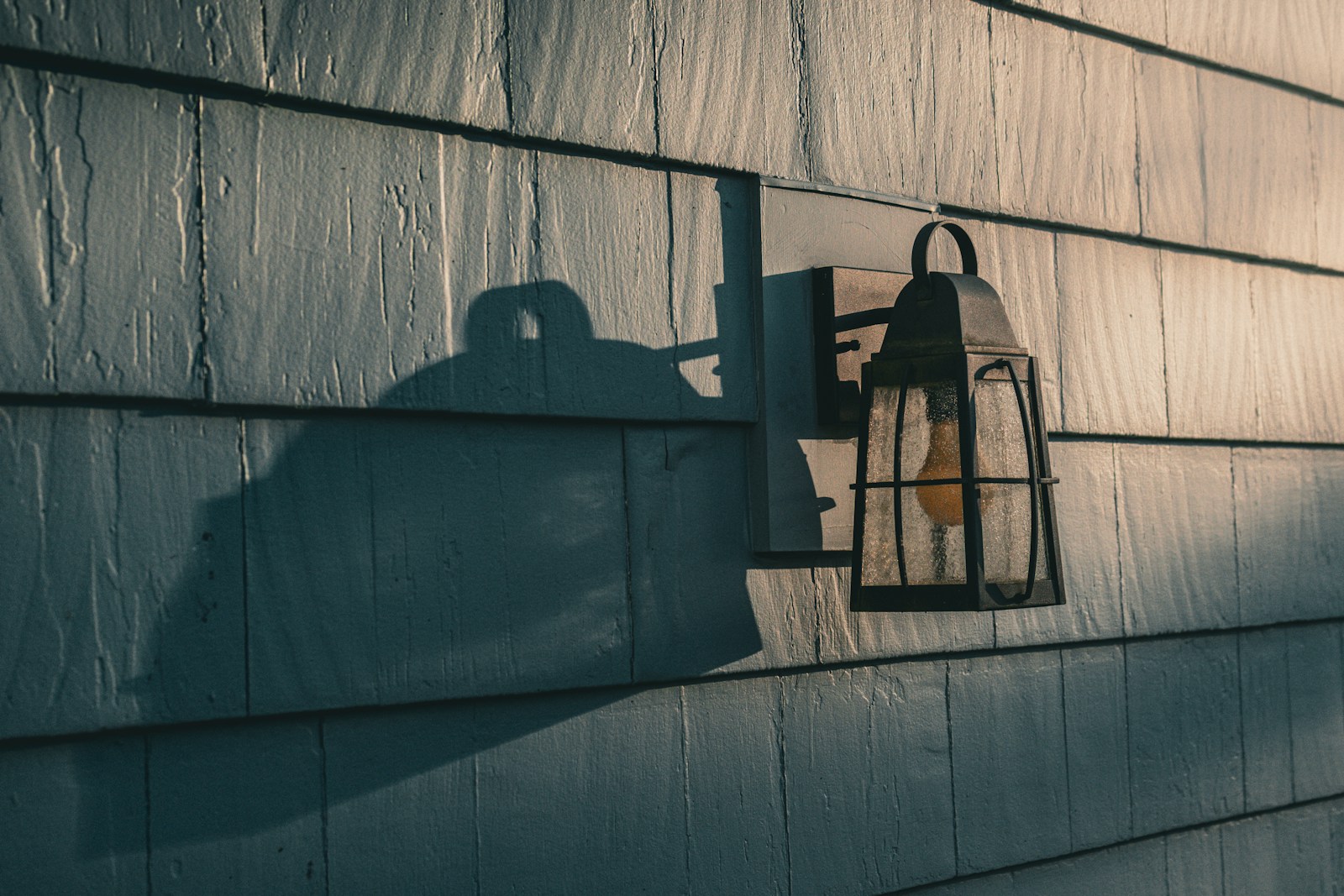 Outdoor lantern casts a shadow on a clapboard wall