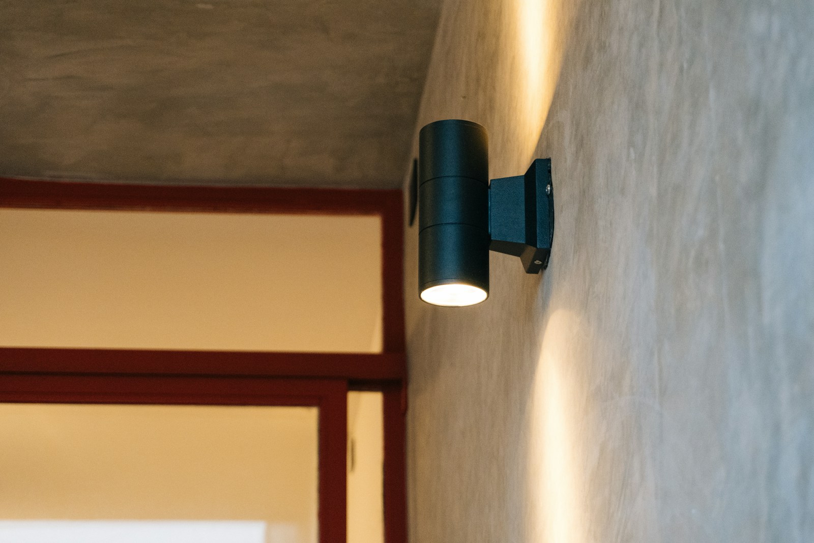 A modern black outdoor wall light illuminates concrete wall