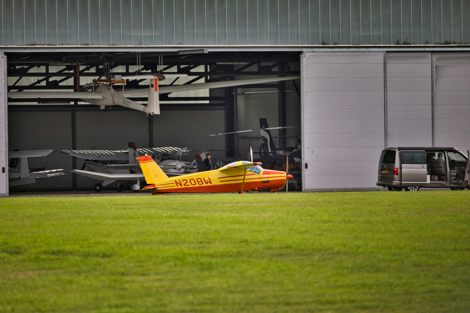 Small airplane parked in an open hangar with a van