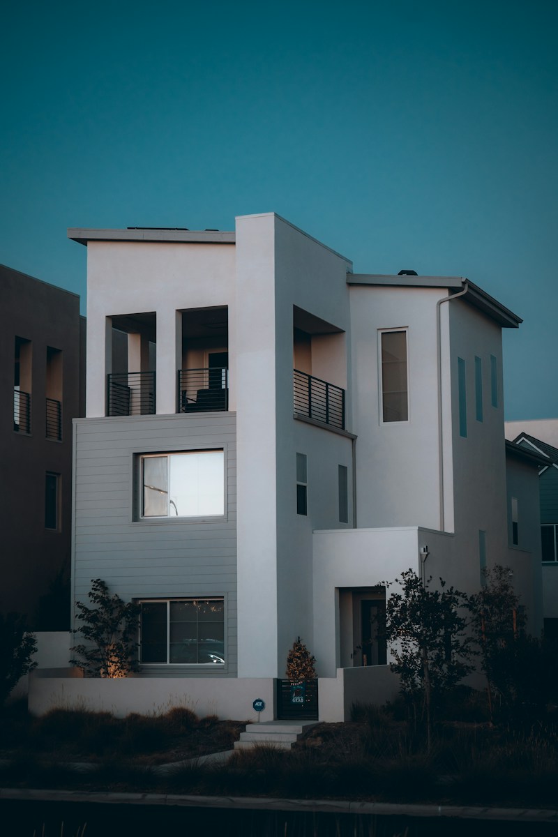 A modern three-story house with white walls and grey siding at dusk