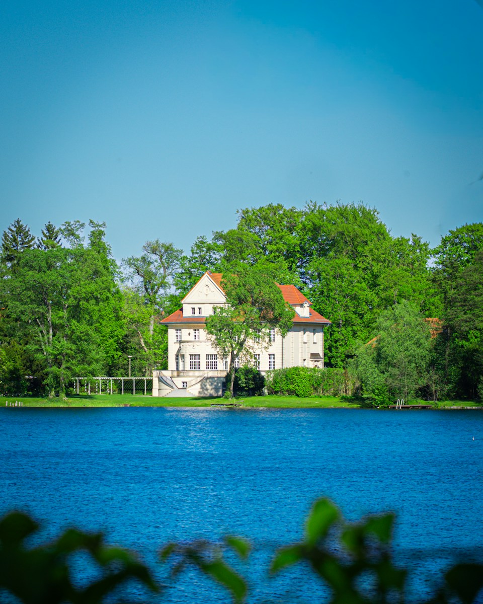 White house with red roof by blue lake and trees