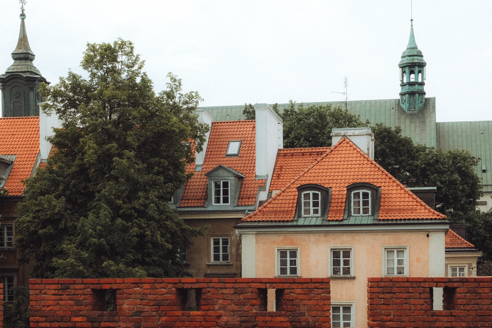 Picturesque view of historic Warsaw buildings and lush trees against an overcast sky.