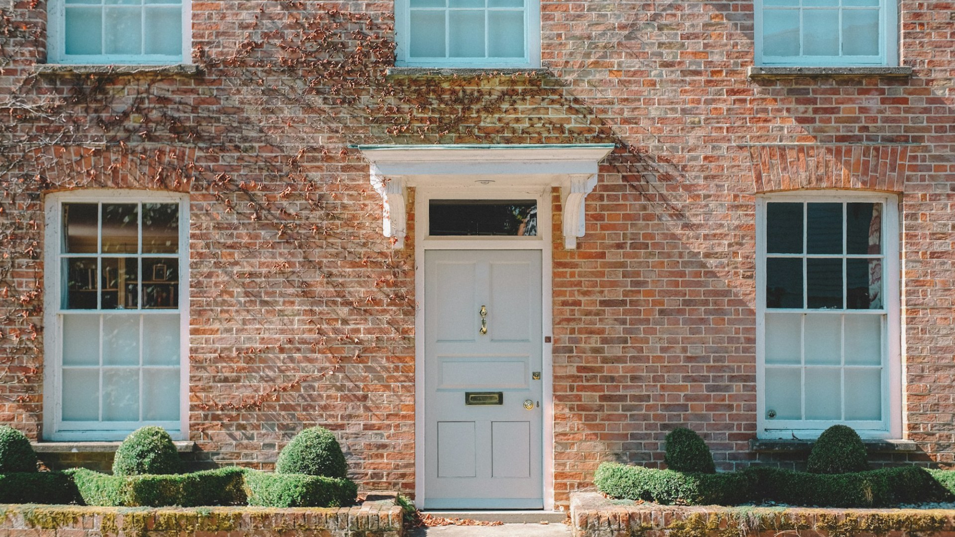 A brick house with a white front door. Photo by Viktor Forgacs on Unsplash.