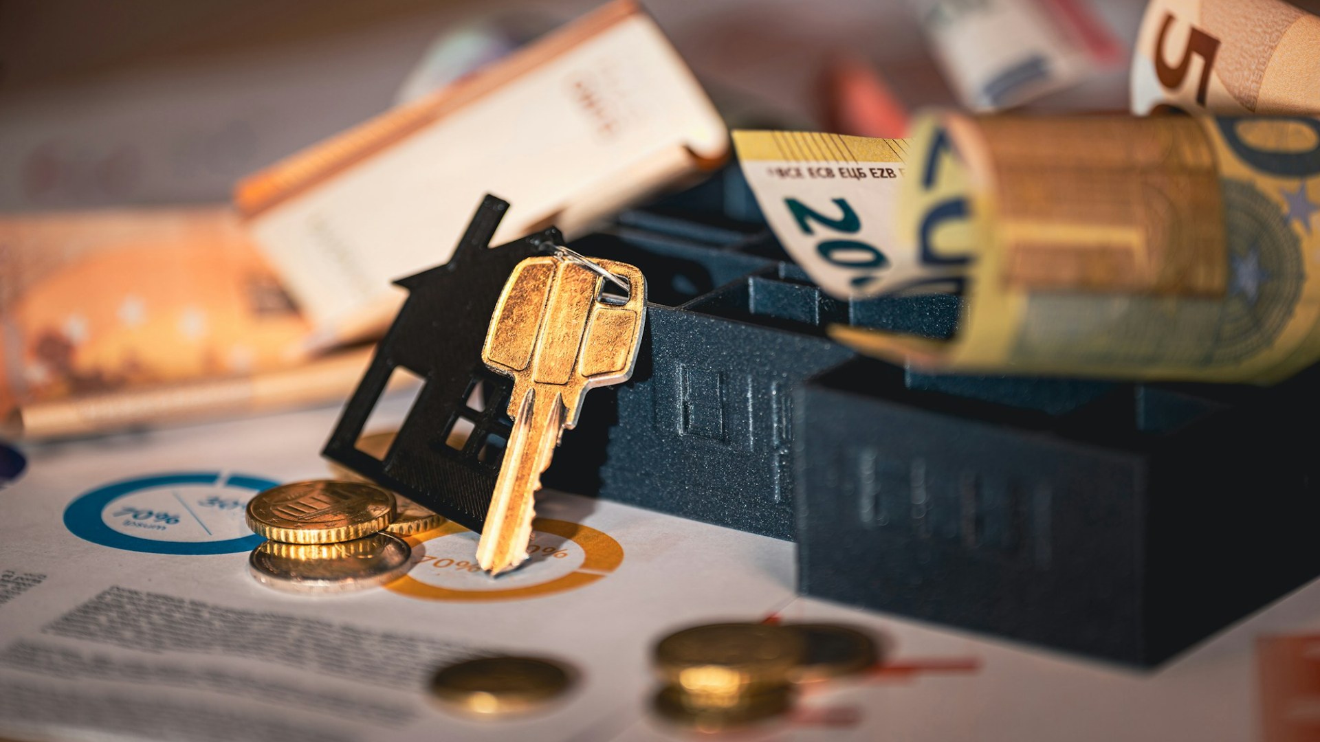 A house model, door keys, a mortgage agreement and coins on a table. Photo by Jakub Żerdzicki on Unsplash.