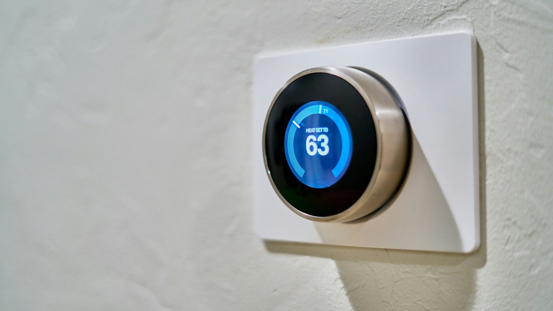 A gray wall thermostat displaying 63 degrees. Photo by Dan LeFebvre on Unsplash.