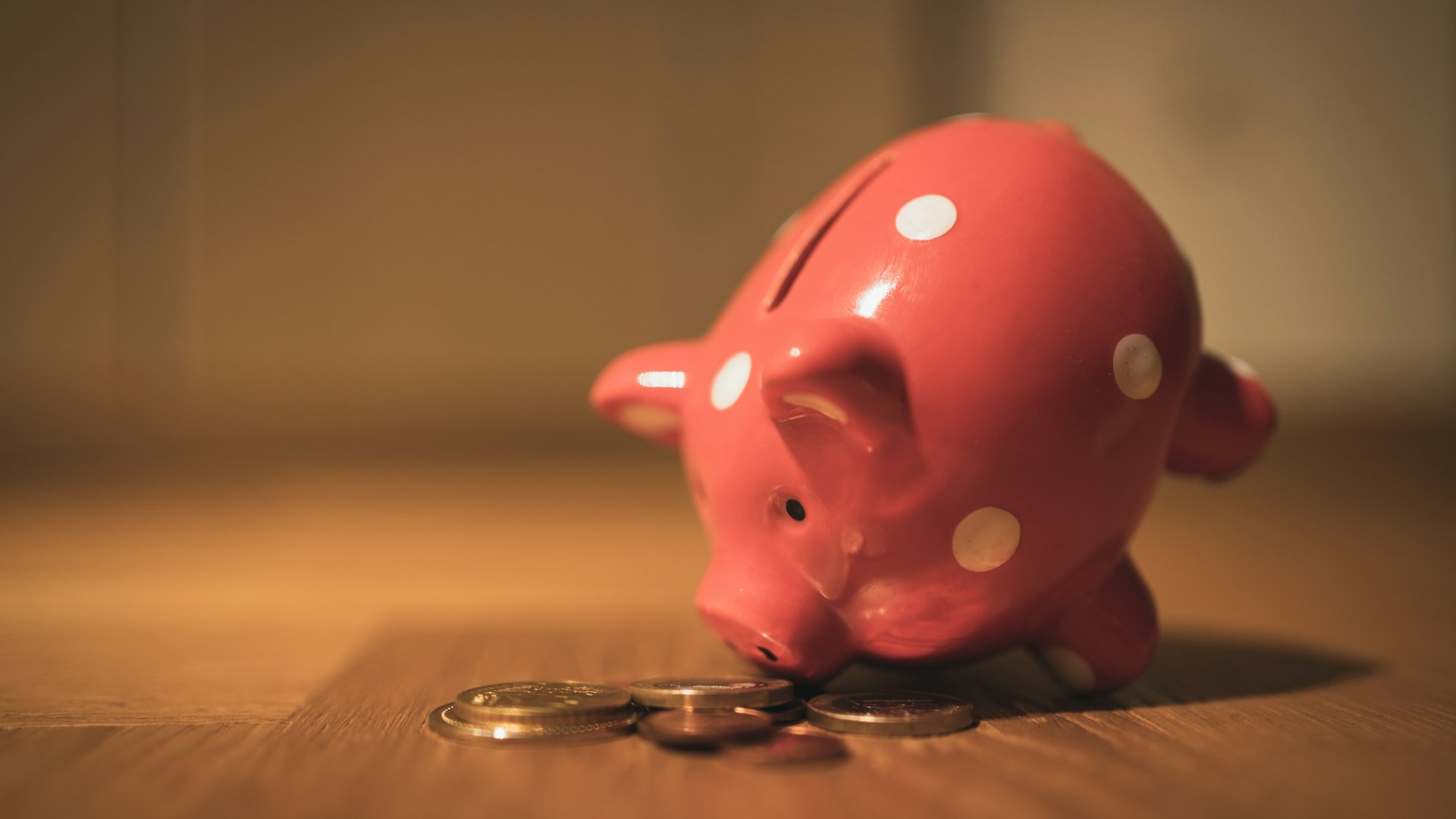 A pink piggy bank with coins on a wooden table. Photo by Andre Taissin on Unsplash.