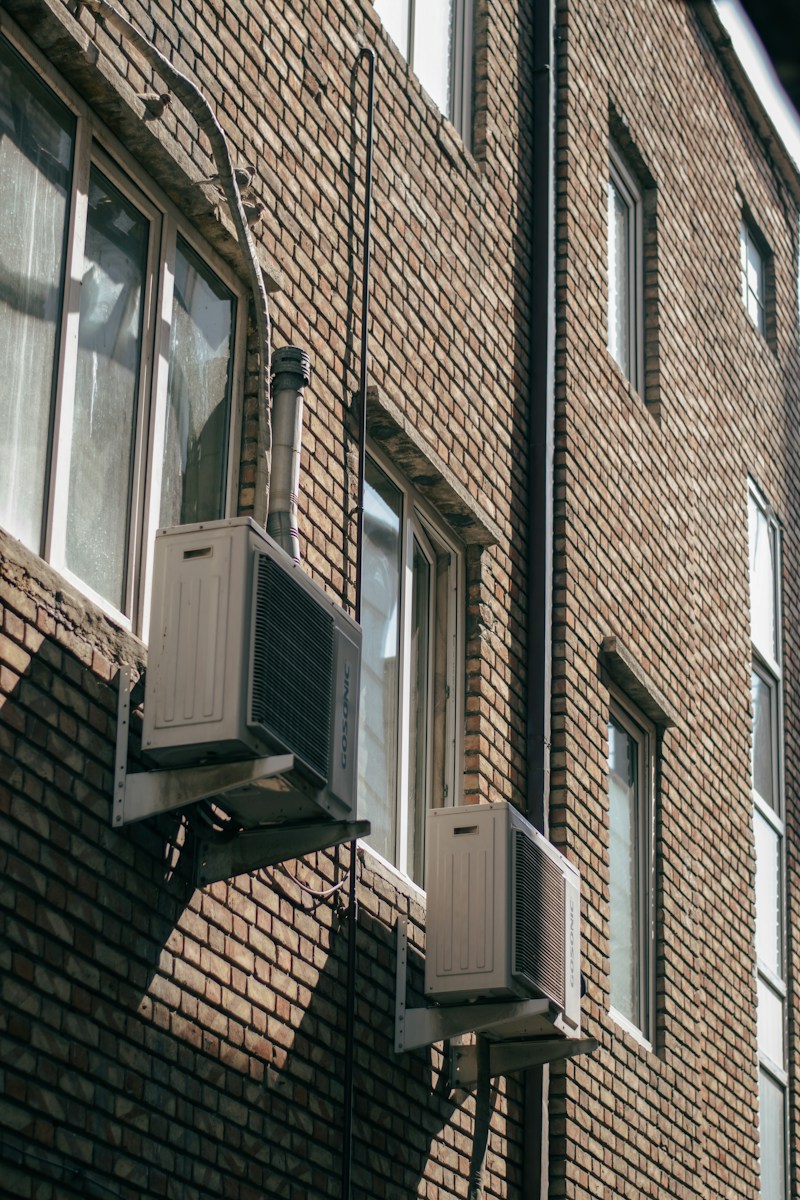 Two air conditioning units on a brick building wall